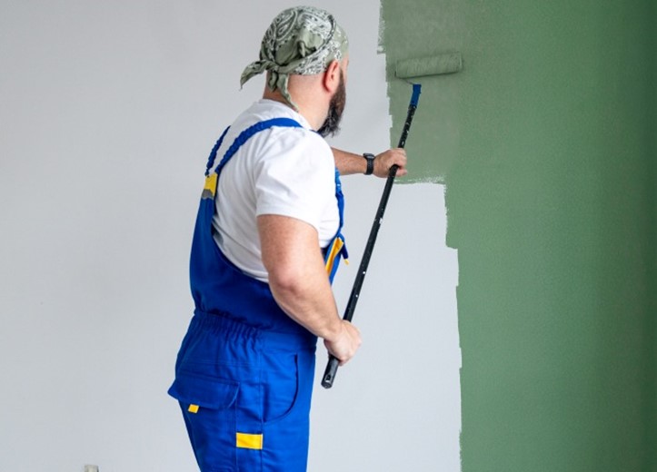 A man dressed in overalls paints a green fence in Atlanta and Kennesaw, GA